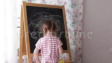 小学前女孩在黑板上写字。 幼儿女孩拿着粉笔画画。